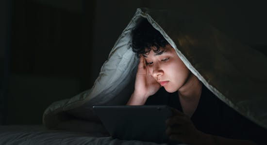 Teenage girl using smartphone in bed late at night with sad facial expression. Horizontal composition.