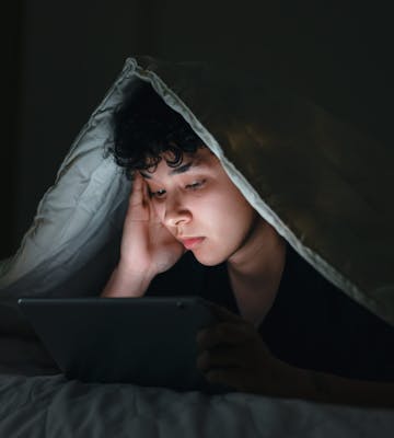 Teenage girl using smartphone in bed late at night with sad facial expression. Horizontal composition.